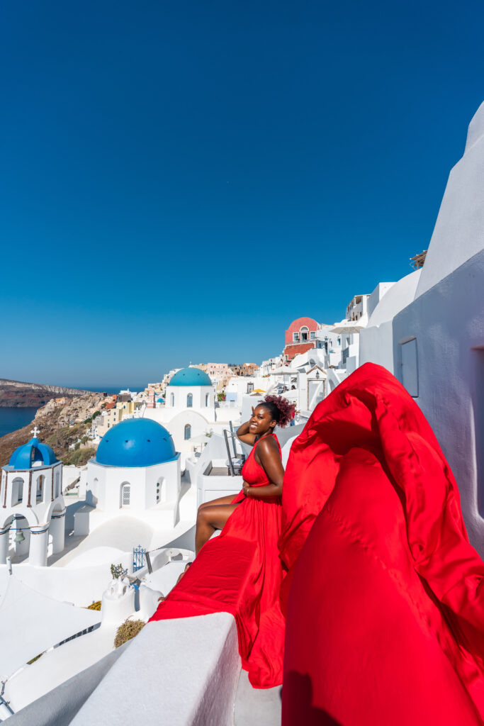 A Black woman in a red dress doing the Flying Dress in Santorini photoshoot