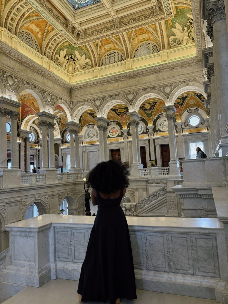 Black woman with large fro and long black dress staring at the walls of the Library of Congress