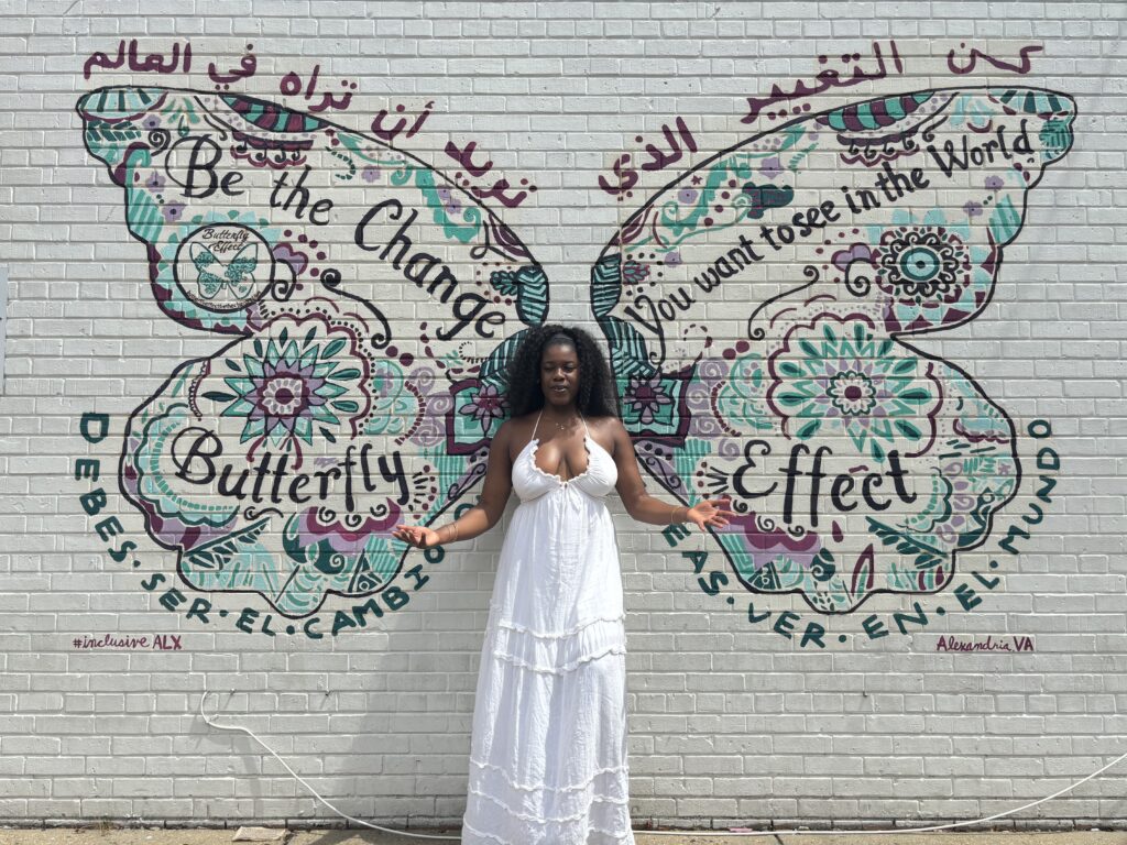 a Black woman in a white dress in front of a butterfly street art mural