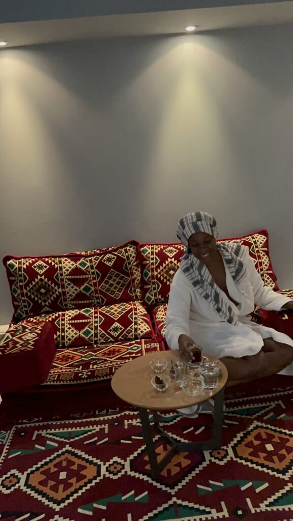 dark skinned Black woman sitting on a Moroccan couch at a spa in robe 