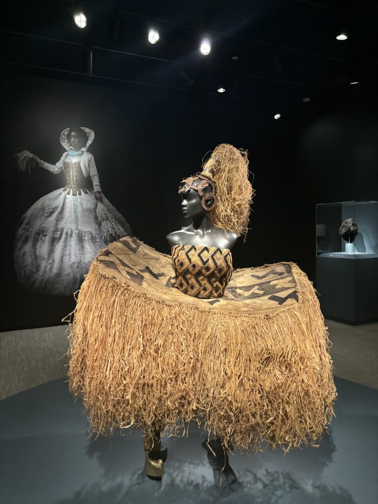 a sculpture of a African woman in an oversized raffia skirt and top