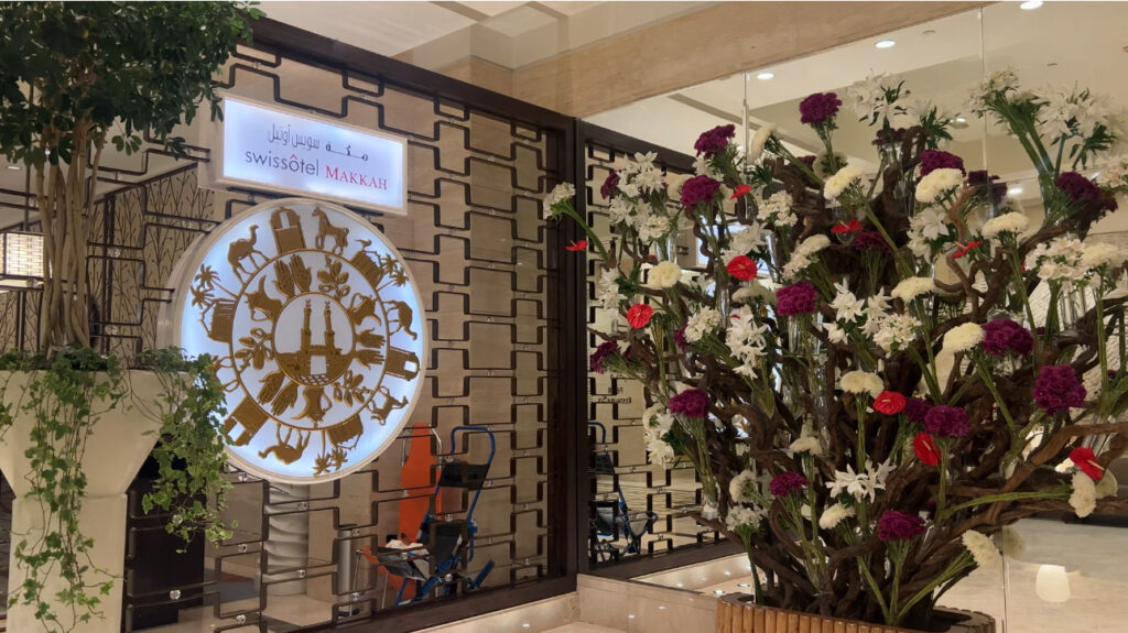 a wooden carved door with a sign that says Swissotel Makkah. A large bouquet of flowers are next to it