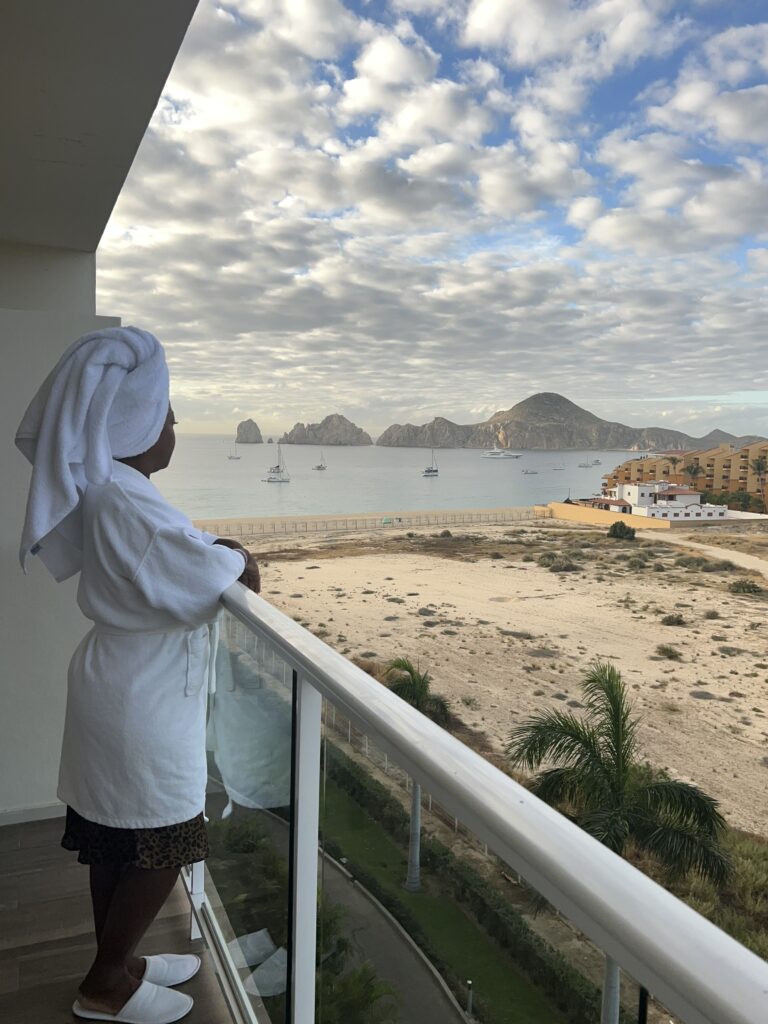 A Black woman in a robe and towel headwrap staring at the ocean 