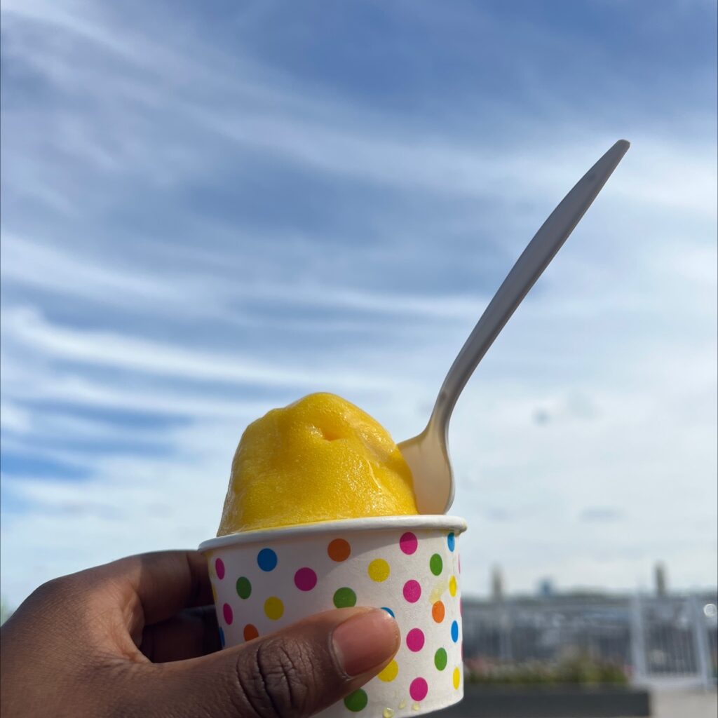 a Black woman holding a yellow sorbet up to the sky 