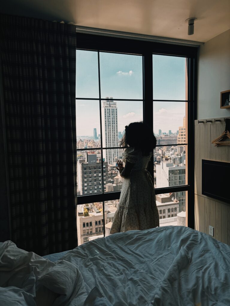a silhouette of a Black woman with afro staring out a tall high rise window during the day