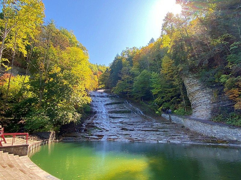 Buttermilk Falls leads into a pool surrounded by green and orange foliage 