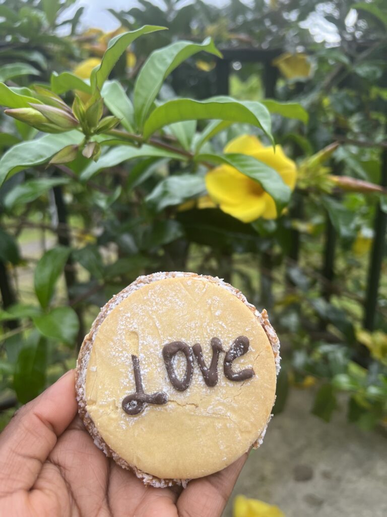 A Black woman holding a Alfajores (Dulce de Leche Sandwich Cookies), with love written in chocolate on the top 