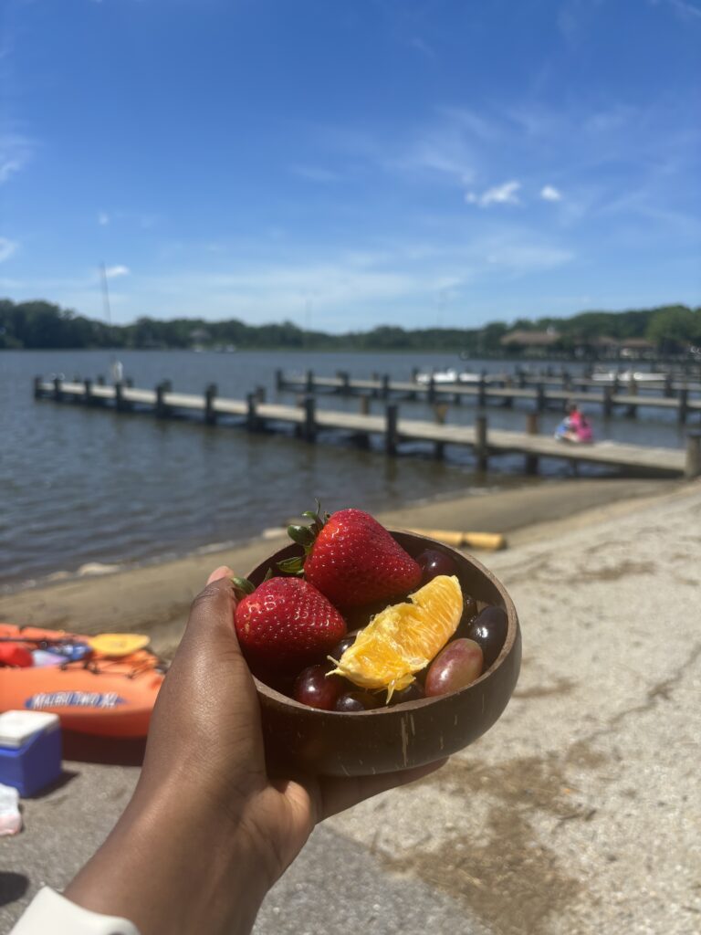 a Black woman holding a coconut bowl of fruit by Sandy Point Beach, a beach near DC