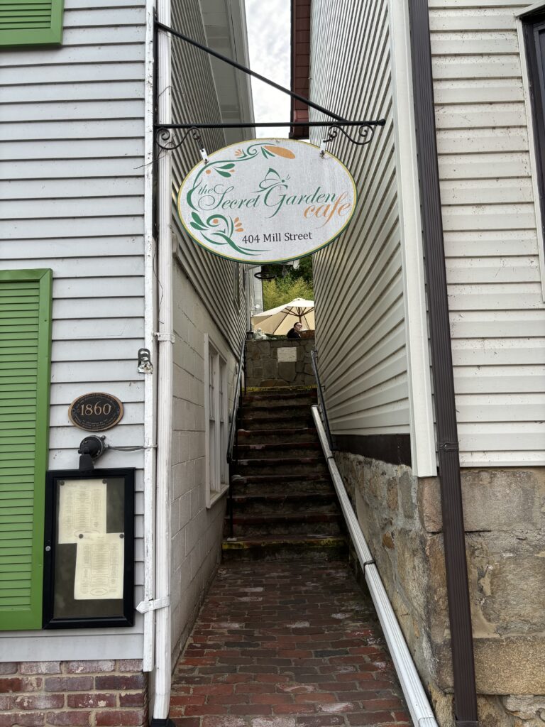 a sign that says "Secret Garden Cafe" in a small alleyway