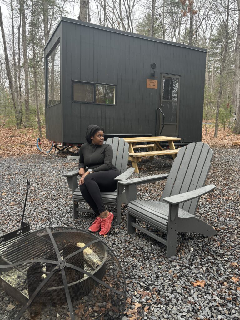 Black woman sitting in front of fire place and tiny home during the day