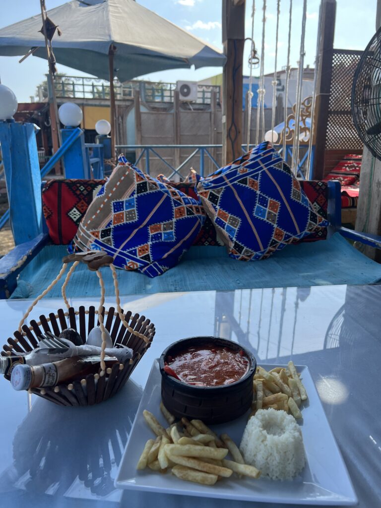 traditional and colorful Egyptian restaurant bench and pillows, vegetarian stew, rice, and fries on table at a outdoor restaurant in Dahab
