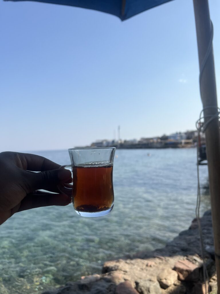 a Black woman holding a  cup of Egyptian tea with the ocean in the background