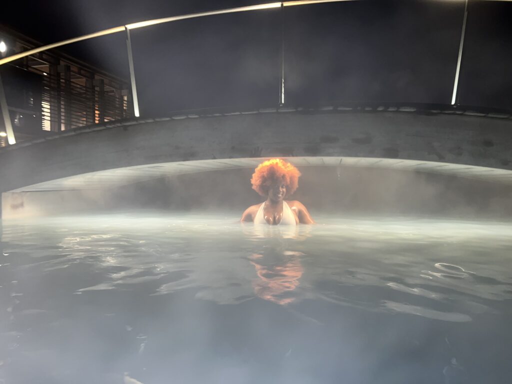 a Black woman with ginger fro standing under a bridge in the Blue Lagoon in Iceland at night
