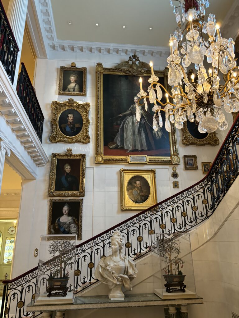 the entry hall is filled with luxurious portraits of family members and historical figures in front of a grand staircase
