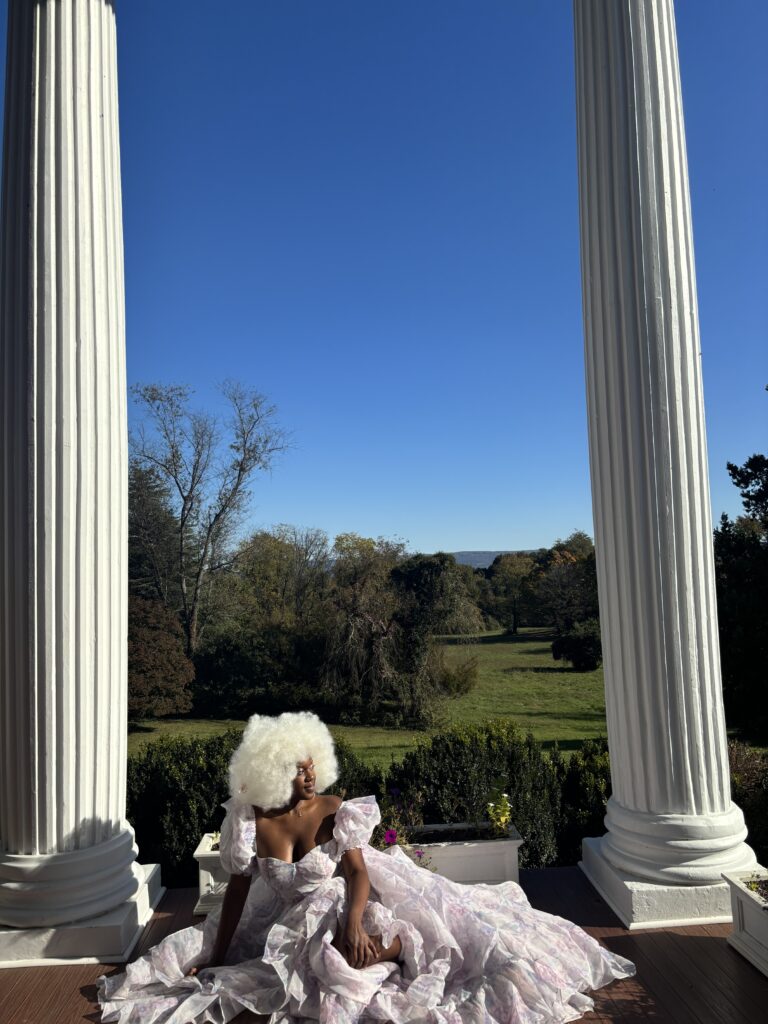 Dark skinned Black woman wearing a dramatic Selkie dress between two white columns 