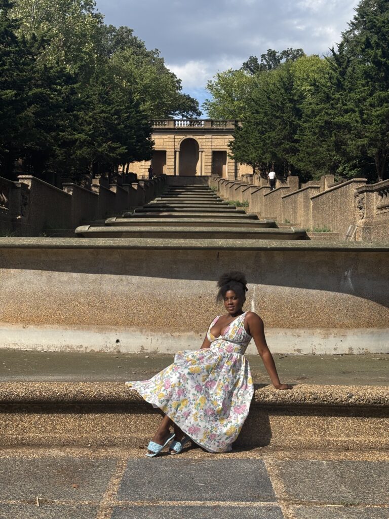 Black woman with white dress with flowers sitting in front of a waterfall in Meridian Hill in DC during the fall 