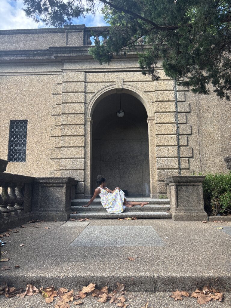 Black woman wearing a flower printed dress in front of gothic styled wall in Meridien Hill Park 