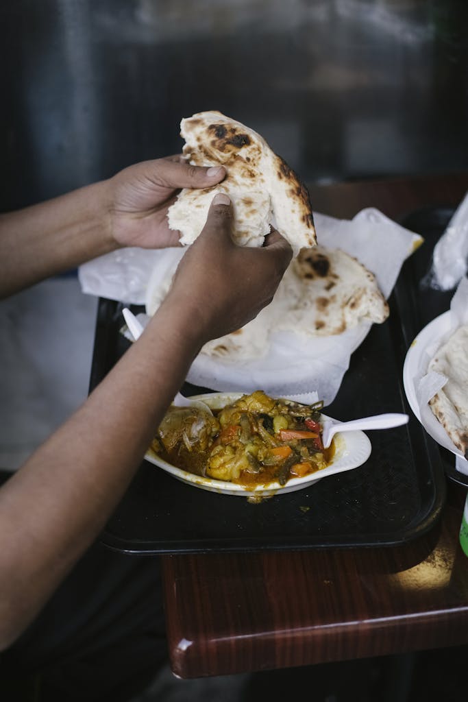 High angle of crop faceless ethnic male eating curry with roti bread at table in cafe