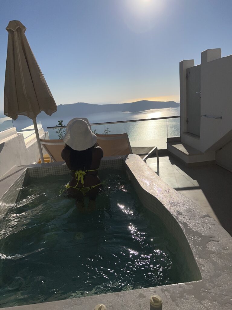 a dark skinned women in a bathing suit in a villa front pool in a luxury hotel in Santorini