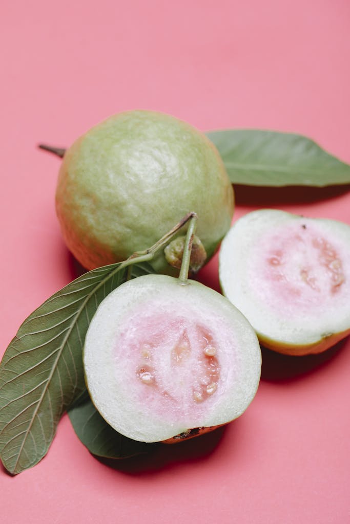 From above ripe fresh appetizing cut in half and whole fruits of guava on pink surface