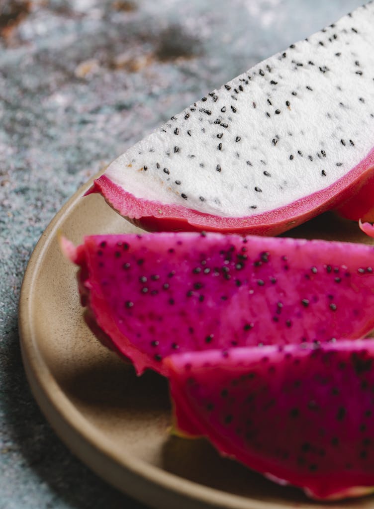 Pieces of ripe tasty dragon fruit with pink and white flesh served on round plate on marble table in kitchen