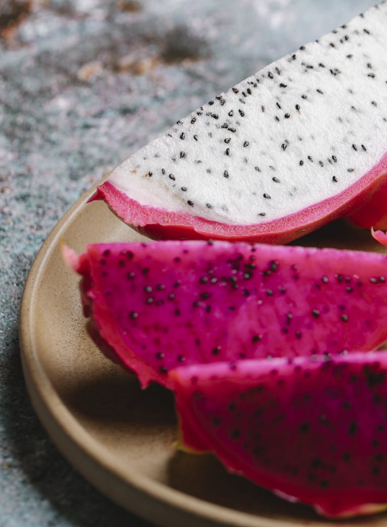 Pieces of ripe tasty dragon fruit with pink and white flesh served on round plate on marble table in kitchen