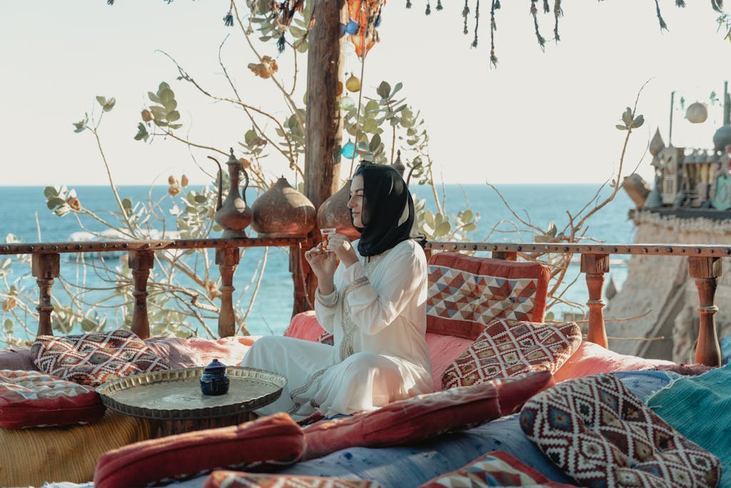 Woman in White Abaya And Black Hijab Sitting With View Of The Sea