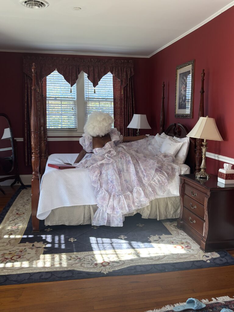 Black woman in selkie dress sitting on a vintage bed at Rosemont Manor