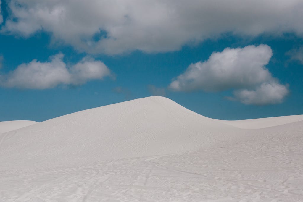 From below of pure blue sky with clouds over empty endless desert landscape with wheels and shoes tracks on surface