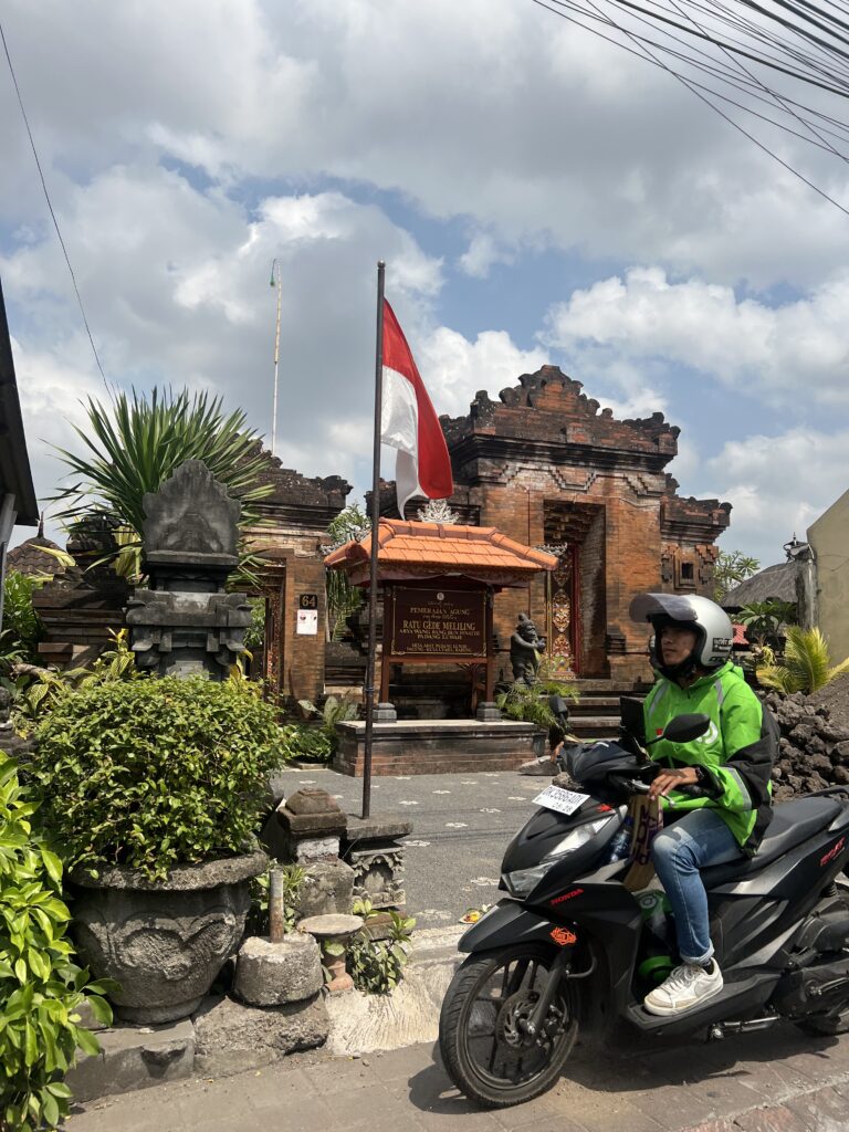 a man on a Gojek bike in Kuta Bali in front of a temple