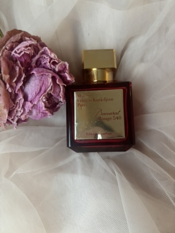 a bottle of Baccarat rouge on pink tulle fabric, next to a dried pink rose