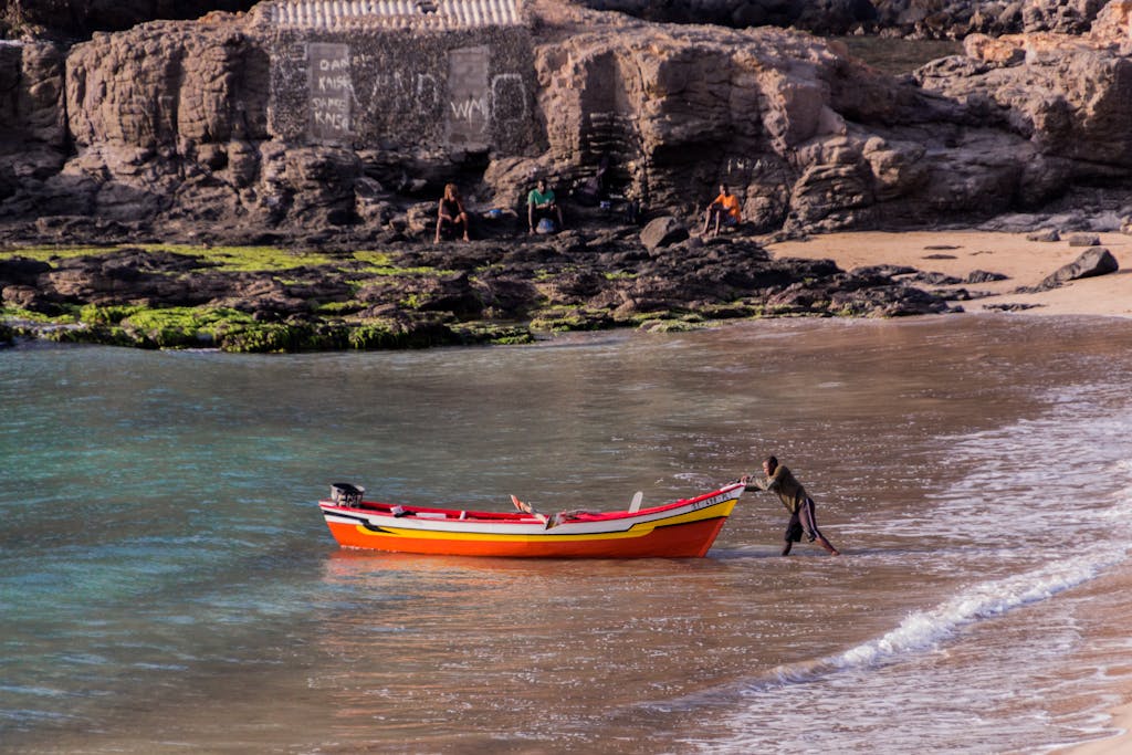 A fisherman pushes a colorful boat towards the shore of Tarrafal Beach in Cape Verde.