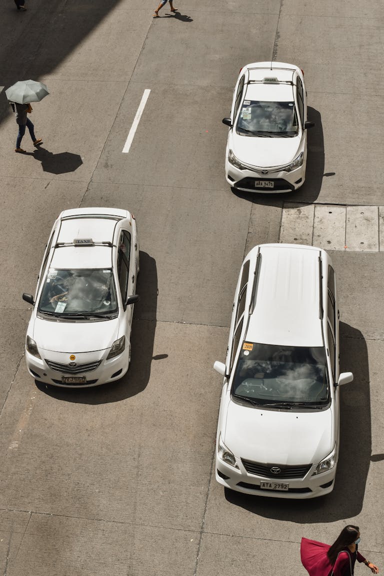 Traffic scene with white cars and pedestrians on a city street in Manila, Philippines, captured from above.